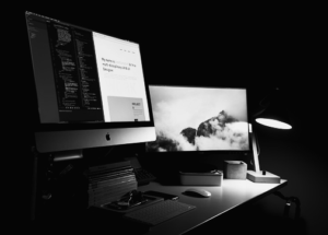 A modern desk setup with two monitors, a keyboard, and various office supplies is illuminated by a desk lamp in a dark room—perfect for late-night digital marketing or SEO work.