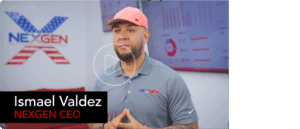 Ismael Valdez, in a pink cap and gray NEXGEN polo shirt, stands before a screen displaying digital marketing graphs and charts, with prominent "NEXGEN" branding in the background.