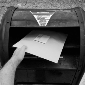 A person places a large envelope into a public mailbox with an "Attention" warning label on the lid, perhaps mailing important crm or email marketing documents.