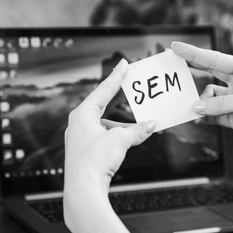 A person holds a note with "SEM" written on it in front of an open laptop, highlighting the importance of search engine optimization in digital strategies.