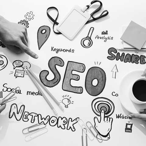 A desk with hands pointing at SEO-related doodles and words like "marketing," "website," and "analysis," surrounded by office supplies and a cup of coffee.