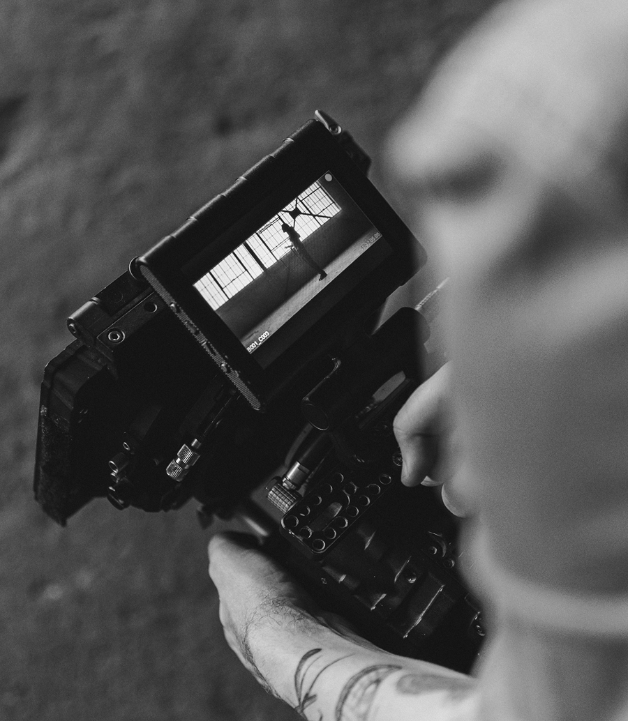A person operates a camera, with the screen displaying a black-and-white image—perfect for digital marketing—of someone standing before large windows inside an industrial space.