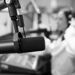 A close-up of a microphone in a radio studio, with a blurred person operating audio equipment in the background—capturing the broadcast energy that can inspire marketing and email marketing strategies.