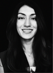 Black and white portrait of a woman with long dark hair, smiling, wearing a necklace and dark top against a black background—perfect for showcasing professionals in marketing or search engine optimization.