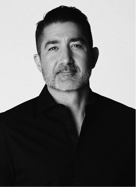 A man with short dark hair and a beard, dressed in a dark collared shirt, looks at the camera against a plain light background, projecting confidence often seen in digital marketing professionals.