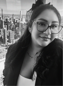 A woman with glasses and long dark hair stands in front of a city skyline, wearing a blazer and a necklace. The black and white photo captures her confidence—perfect for presenting a professional in marketing or search engine optimization.