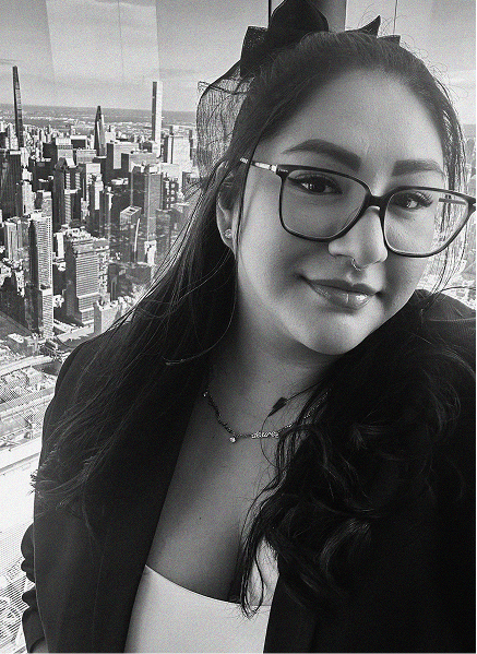 A woman with glasses and long dark hair stands in front of a city skyline, wearing a blazer and a necklace. The black and white photo captures her confidence—perfect for presenting a professional in marketing or search engine optimization.