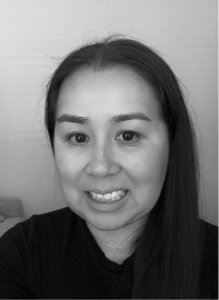 A woman with long, straight hair smiles at the camera, embodying confidence. She is wearing a dark top in a plain indoor setting. The black and white photo exudes a professional vibe—perfect for marketing or SEO profiles.