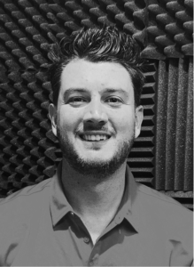 A man with short dark hair and a beard smiles at the camera, standing in front of a wall covered in soundproof foam panels—ready to tackle digital marketing or share his latest SEO strategies.