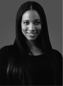 A woman with long straight hair and a dark top smiles at the camera against a plain, dark background, capturing the confident spirit of an email marketing professional.