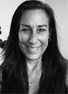 A woman with long dark hair and a necklace smiles at the camera in a black and white portrait, capturing the professional confidence often seen in marketing campaigns.