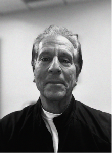 Black and white photo of an older man with short, combed-back hair, wearing a dark jacket over a white shirt, facing the camera in an indoor setting—perfect for a professional profile on CRM or email marketing platforms.