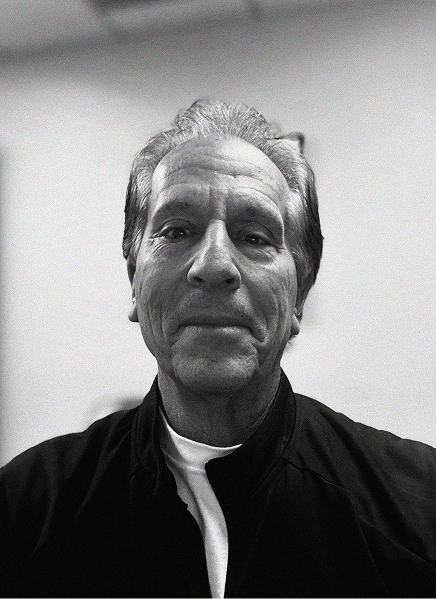 Black and white photo of an older man with short, combed-back hair, wearing a dark jacket over a white shirt, facing the camera in an indoor setting—perfect for a professional profile on CRM or email marketing platforms.