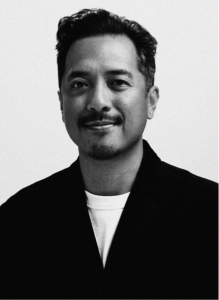 A man with short, dark hair and facial hair, wearing a dark jacket over a light shirt, smiles slightly while facing the camera against a plain background—exuding confidence often seen in digital marketing professionals.
