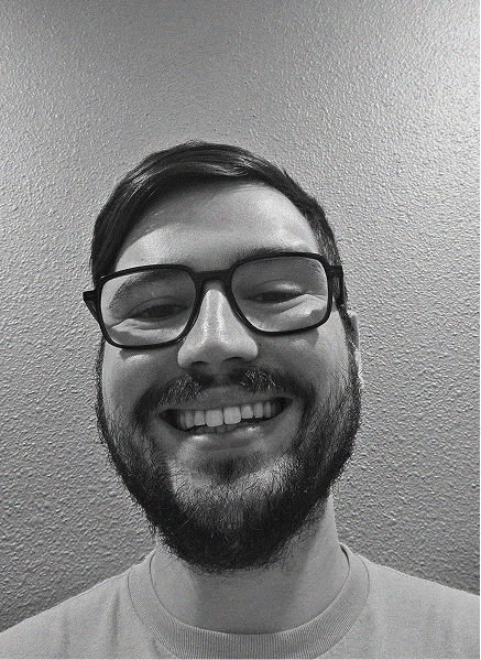 A person with glasses and a beard, perhaps a digital marketing expert, smiles at the camera in front of a textured wall. The image is in black and white.