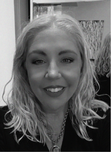 A woman with wavy light hair smiles at the camera, wearing a necklace and dark top, with a blurred background behind her—perfect for marketing or SEO profile images.