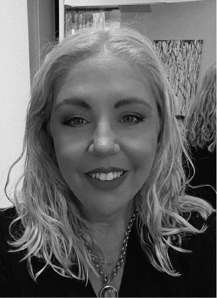 A woman with wavy light hair smiles at the camera, wearing a necklace and dark top, with a blurred background behind her—perfect for marketing or SEO profile images.