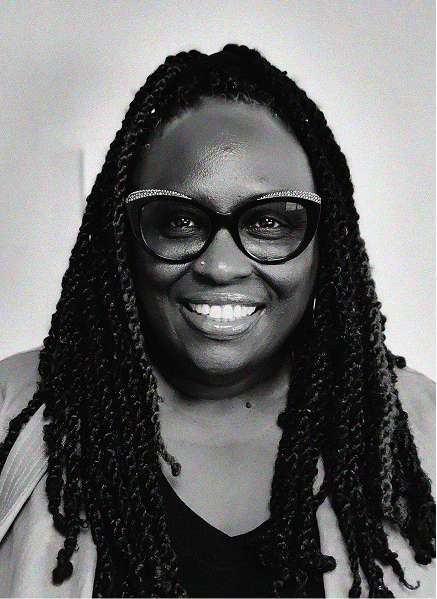 A woman with long braided hair, wearing dark-rimmed glasses and a dark top, smiles at the camera against a plain background, reflecting confidence in digital marketing.