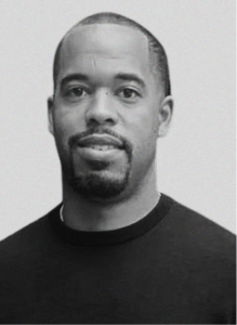 Black and white portrait of a man with short hair, trimmed beard, and mustache, wearing a dark crew-neck shirt, facing the camera against a plain background—ideal for digital marketing or CRM profile use.