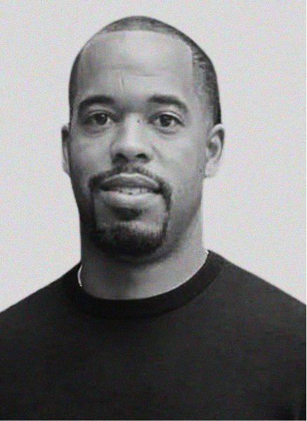 Black and white portrait of a man with short hair, trimmed beard, and mustache, wearing a dark crew-neck shirt, facing the camera against a plain background—ideal for digital marketing or CRM profile use.