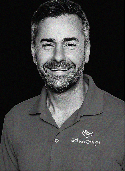 A man with short hair and a beard smiles, wearing a polo shirt with the "ad leverage" logo, representing expertise in marketing, against a black background.