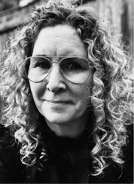 Black and white portrait of a person with curly hair and large glasses, looking at the camera with a slight smile. A wooden fence is visible in the blurred background, evoking a thoughtful mood perfect for marketing or CRM campaigns.