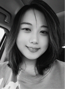 A person with shoulder-length hair and a light-colored shirt smiles at the camera while sitting inside a car. The black and white image gives this digital marketing professional a timeless and approachable look.