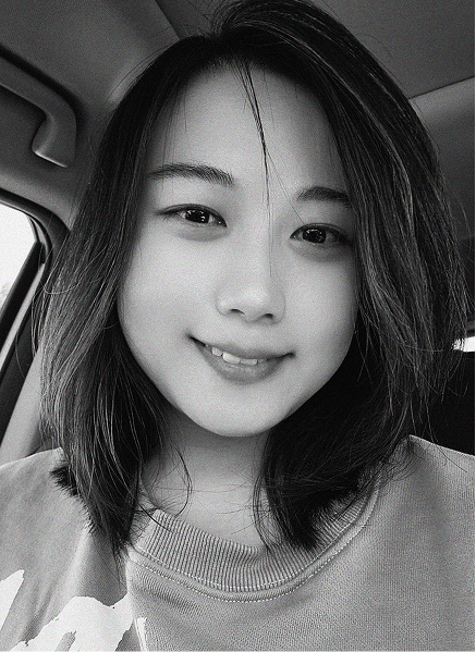 A person with shoulder-length hair and a light-colored shirt smiles at the camera while sitting inside a car. The black and white image gives this digital marketing professional a timeless and approachable look.