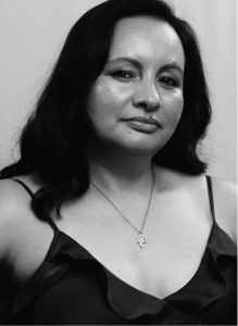 Black and white portrait of a woman with long dark hair, wearing a sleeveless top and a necklace, looking directly at the camera with a neutral expression—capturing the focus and clarity essential in successful marketing.
