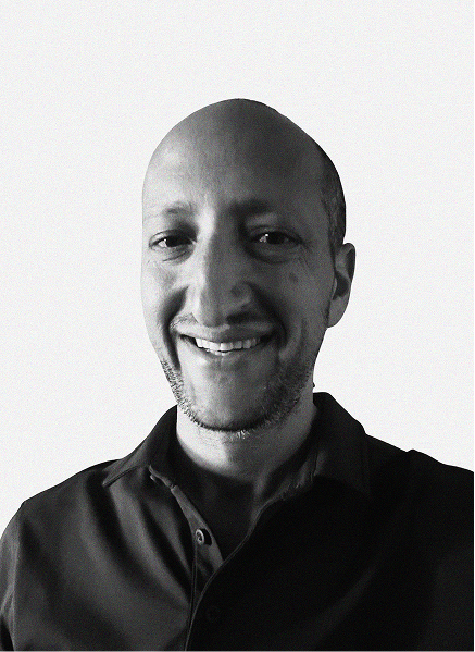 A man with a shaved head and short beard smiles at the camera while wearing a dark collared shirt against a plain background, reflecting confidence often seen in digital marketing professionals.