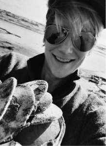 Person wearing sunglasses and a cap smiles while holding several large, sandy clams on a beach—celebrating a digital marketing win as bright as the summer sun.