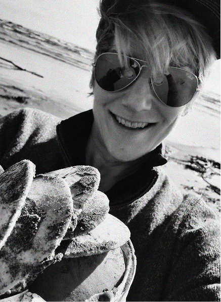 Person wearing sunglasses and a cap smiles while holding several large, sandy clams on a beach—celebrating a digital marketing win as bright as the summer sun.