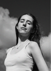 Black and white photo of a woman with long hair wearing a sleeveless top, standing outdoors beneath a cloudy sky, evoking the creativity behind marketing campaigns.