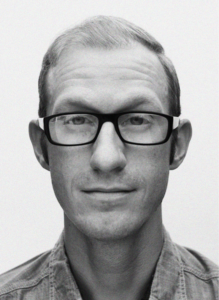 A man with short, light hair wearing black glasses and a button-up shirt looks directly at the camera against a plain background—perfect for showcasing digital marketing or CRM expertise.