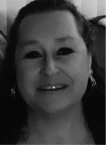 Black and white photo of a person with long curly hair, smiling, wearing hoop earrings and a dark top, seen from the shoulders up—a portrait that captures the creative spirit behind digital marketing.